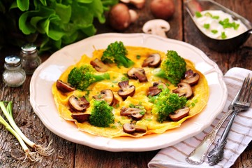 Scrambled eggs with mushrooms, broccoli, cheese and green onions on an old wooden table. Rustic style.