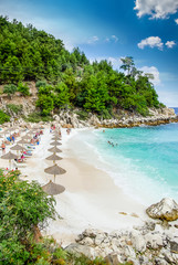 Marble beach (Saliara beach), Thassos Islands, Greece. The most beautiful white beach in Greece. Tourists enjoying a nice day at the beach. Straw umbrellas (straw parasol) and sunbeds on the beach.