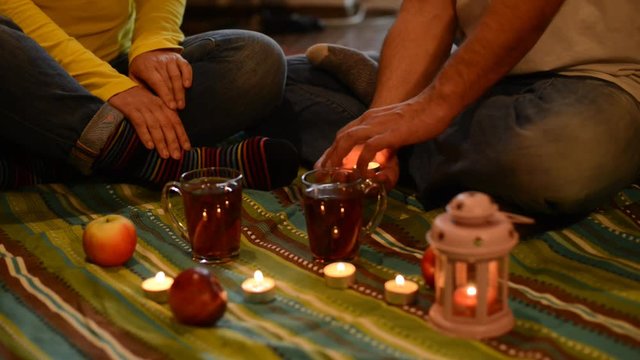 Couple on a romantic date, sitting on the floor, among a candles. Man holds in his hands a candle and handing it to the woman as a symbol of the soul.