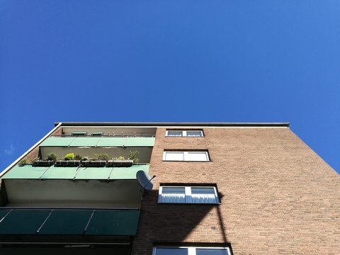 Hochhaus mit brauner Klinkerfassade und gr&uuml;nen Balkons mit Wohnungen und Paraments vor blauem Himmel im Sonnenschein im Hafenviertel oder Hansaviertel in M&uuml;nster in Westfalen im M&uuml;nsterland