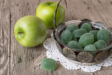 
 Fruit jelly and apples.   Fruit jelly in old vase and two green apples on gray wooden table.
