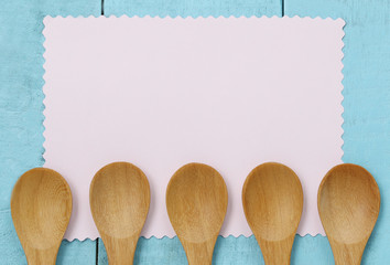 Wooden spoon on pink note paper and blue wood table.