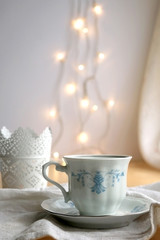 Tea in a vintage porcelain cup and candle holder. Fairy lights in the background. Selective focus.