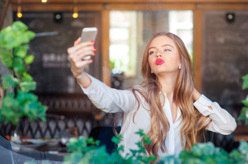Youth and technology. Young beautiful long hair woman taking selfie by smartphone while sitting at cafe.