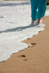 Woman walking on sand beach leaving footprints