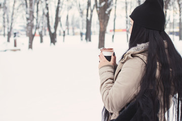 Young woman with takeaway coffee in park in winter. Rear view, unrecognizable person