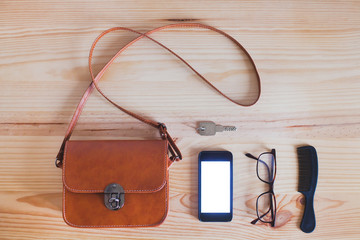 top view of the woman handbag, fashion purse with smartphone, keys and comb on wooden desk