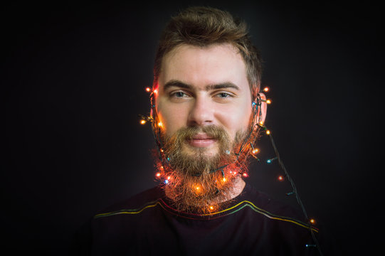 Bearded man smiling. with glowing garland on his head. On a black background.