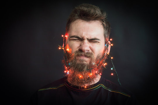 Bearded man fools around. with glowing garland on his head. On a black background.