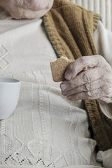 wrinkled hand of a senior person holding coffee and biscuits