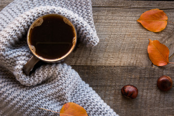 Cup of coffee, cozy knitted scarf, autumn leaves on wooden board. Autumn still life. Vintage style.