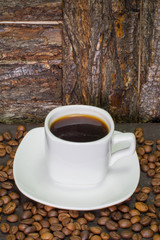 small white cup of coffee, roasted coffee beans on wooden background