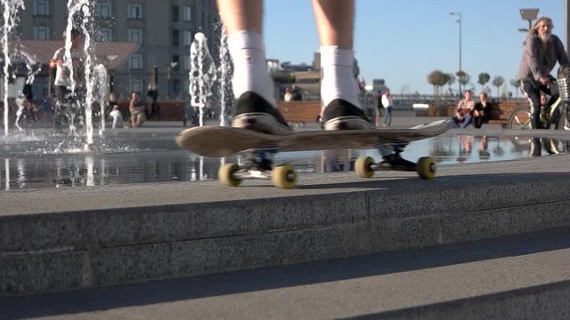 Skateboard moving in slow-mo. People near a fountain. Summer days in open air. Skateboarder in the city.