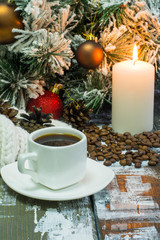 Obraz na płótnie Canvas small white cup of coffee, roasted coffee beans, lighted candle, and fir branch in snow with cone, Christmas decorations on wooden background
