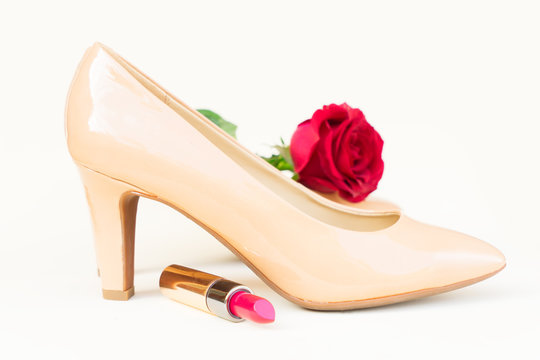 Nude colored high heels still life with red rose flower bud and lipstick