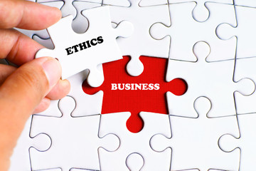 "BUSINESS" word on missing puzzle with a hand hold a piece of "ETHICS" word puzzle want to complete it - business and finance concept