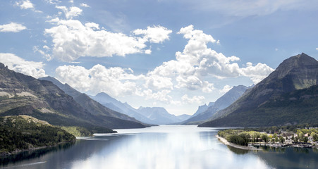 horizontal image of a landscape of a large lake with mountains looming on either side under a bright blue sky with white clouds in the summer time.