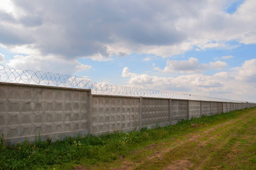Wall with barbed wire on a background of blue sky. long fence