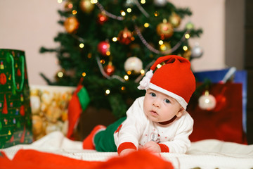Obraz na płótnie Canvas Christmas baby in hat holding red ball near gift box and new year fir tree