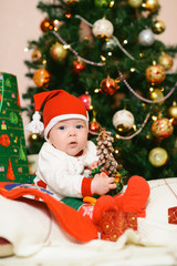 Christmas baby in hat holding red ball near gift box and new year fir tree