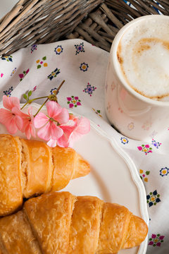 croissants, coffee cup, flower in romantic style on a wicker tra
