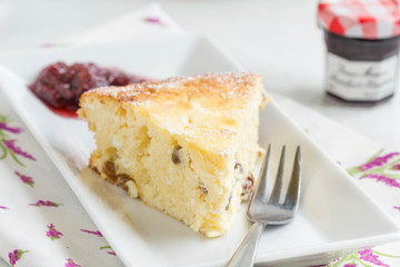 Slice of cottage cheese cake with fruit jam on white plate.