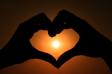 Silhouette of hands in form of heart on background of sunset.