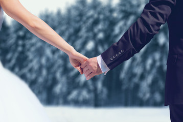 Winter wedding couple, bride and groom holding hands over snowy