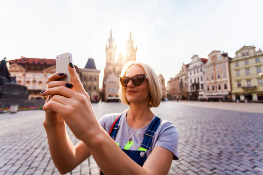 Beautiful young female traveler making self photo on her mobile phone on the background of the Church of Virgin Mary in Old Town Square in Prague. Kostel Panny Marie pred Tynem.