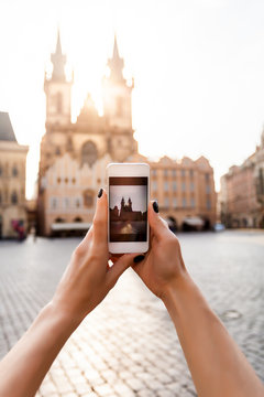 Beautiful young female traveler making photo on her mobile phone of the Church of Virgin Mary in Old Town Square in Prague. Kostel Panny Marie pred Tynem. Phone in hand closeup
