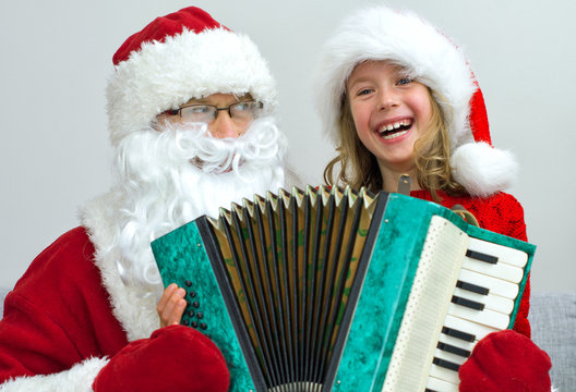 Santa Claus and little girl playing accordion at Christmas.