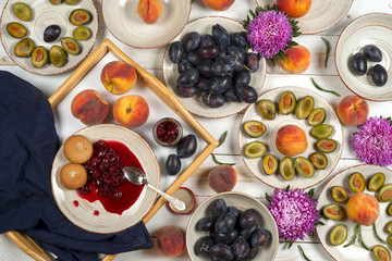 Colorful fruit set of purple, red and orange background in bowls. Plum, peaches, watermelon sliced above white tabletop