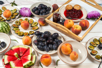 Colorful fruit set of purple, red and orange background in bowls. Plum, peaches, watermelon sliced above white tabletop