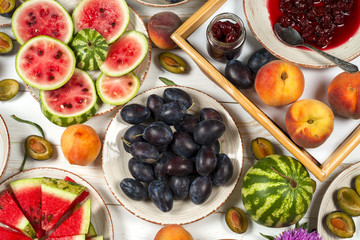 Colorful fruit set of purple, red and orange background in bowls. Plum, peaches, watermelon sliced above white tabletop