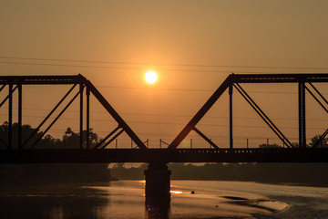 Fototapeta na wymiar A backlit silhouette of a railroad tres-sel on a river at dawn
