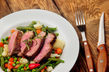 Sliced Beef steak medium rare with asparagus beans,cauliflower,carrot and pea on wooden table.closeup selective focus.Fork and knife