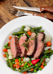 Sliced Beef steak medium rare with asparagus beans,cauliflower,carrot and pea on wooden table.closeup selective focus.Fork and knife