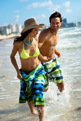 Attractive young couple man and woman playing in surf at South Miami Beach Florida with hotels in...