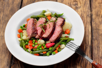 Sliced Beef steak mediu, rare with asparagus beans,cauliflower,carrot and pea on wooden table.closeup selective focus