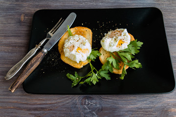 Breakfast - poached eggs on black plate with cutlery, parsley an