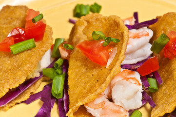 Plantain toco shells filled with shrimp, chopped tomatoes, sliced green onions on a yellow plate