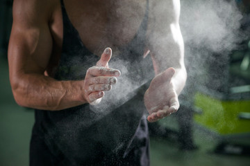 talc on bodybuilding athlete hands on background muscular physique in preparation for training in the gym