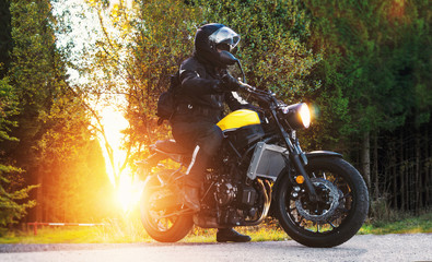 Motorradfahrer auf Landstrasse macht eine Motorradtour im Sonnenuntergang vorm Wald