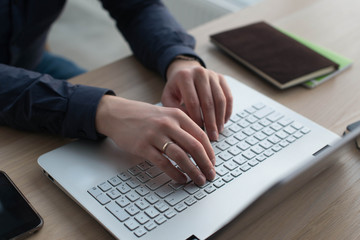 Hands typing on a laptop keyboard. A man works in an office at his workplace