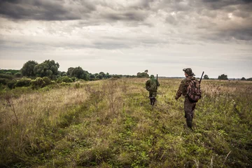 Fototapete Jagd Jäger, die während der Jagdsaison durch ländliches Feld mit dramatischem Himmel gehen