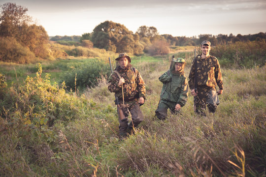 hunters going through tall garass in rural field at dawn during hunting season