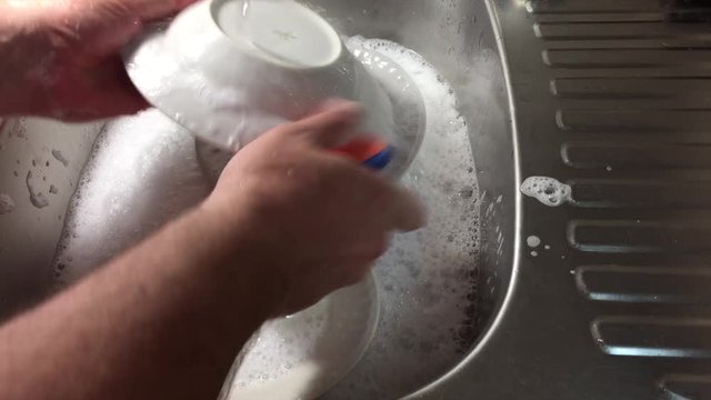 Мужчина моет посуду. Видны руки, тарелки, мойка