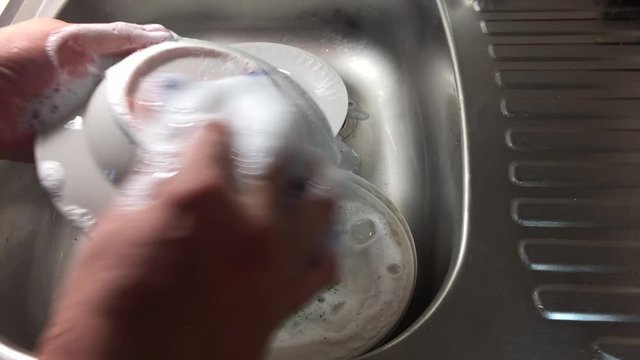 Мужчина моет посуду. Видны руки, тарелки, мойка