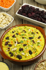 Vegetable couscous in a clay pot and ingredients on a wooden table