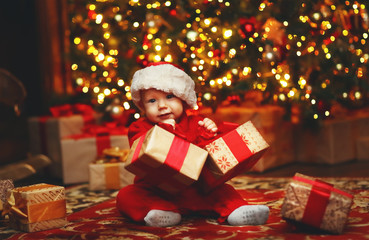 Fototapeta na wymiar Happy baby by Christmas tree with gifts